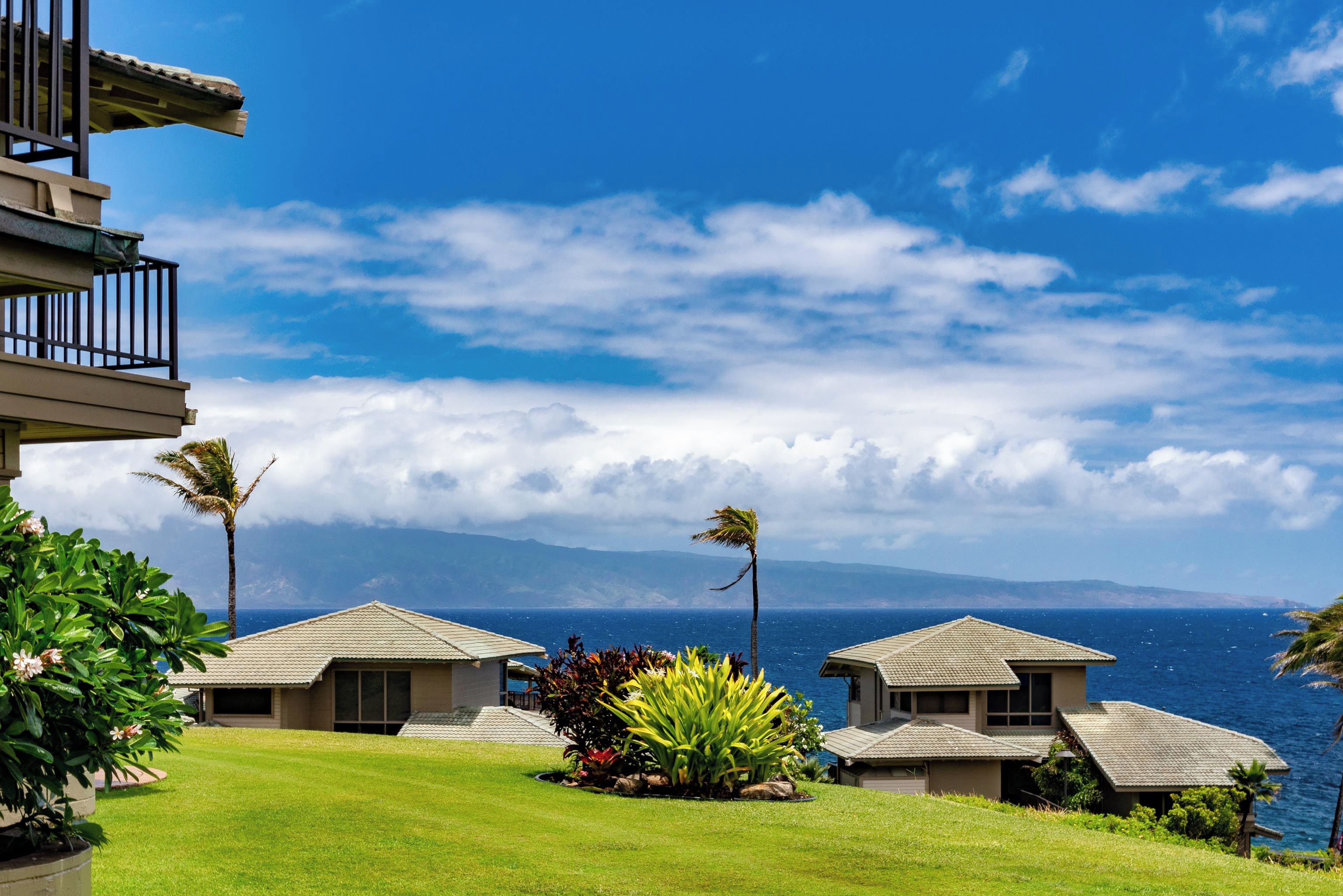 A beachfront property with multiple buildings, a well-maintained lawn, and a view of the ocean.