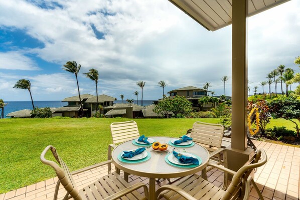 A round table with four chairs, a tropical garden, and a view of the ocean and houses in the background.