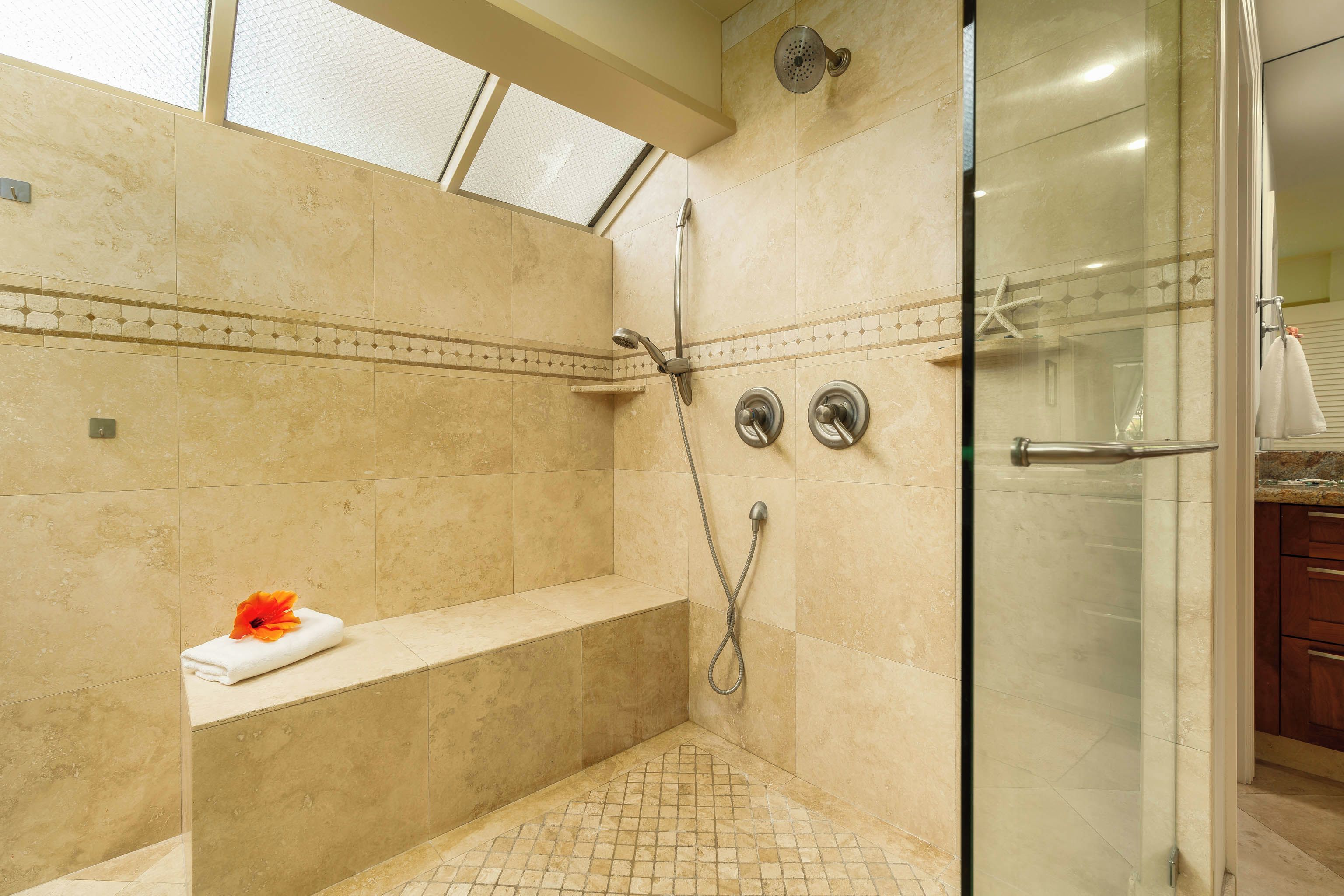 A modern bathroom with a glass shower enclosure, a bench with a towel and flower, and a tiled floor.
