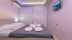 A modern hotel room with a bed, white towels, a grey quilted bedspread, an air conditioning unit, a flat-screen TV, and a wall-mounted picture. - Evia's Apartment   New Apartment In Town! (Zakynthos)