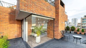 Une terrasse sur le toit, accessible par une porte vitrée, agrémentée de plantes en pot et dotée de sièges d’extérieur.