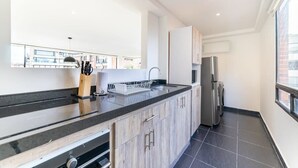 Une cuisine moderne avec un plan de travail noir, des armoires en bois, un réfrigérateur en acier inoxydable et une fenêtre donnant sur l’extérieur.