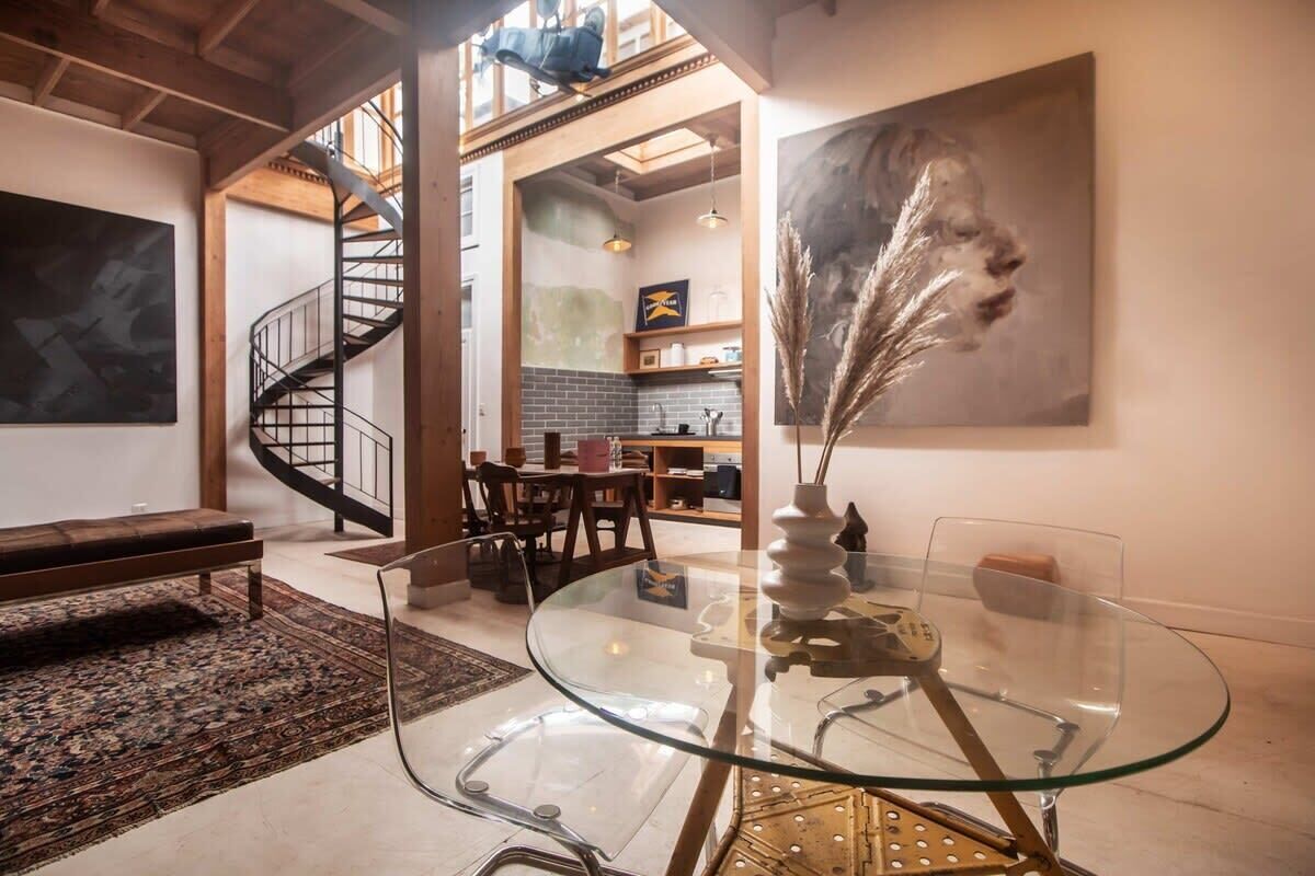 A modern interior with a glass dining table, a spiral staircase, and a large abstract painting.