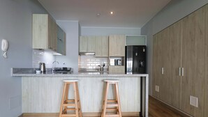 Une cuisine moderne avec des meubles en bois, un réfrigérateur en acier inoxydable et deux tabourets de bar.