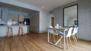Une cuisine moderne avec un plancher en bois, un coin repas avec une table en bois et des chaises blanches, et un grand miroir au mur.