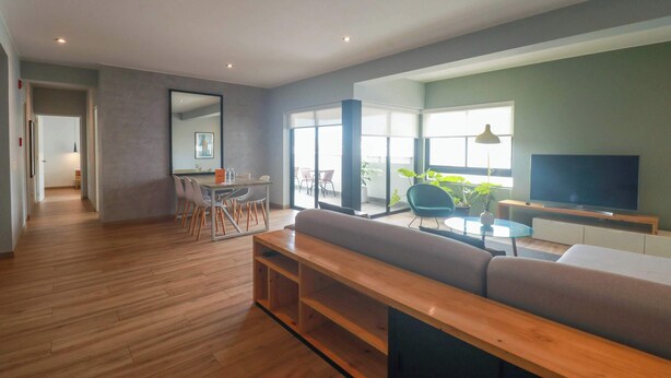 Un salon moderne avec un plancher en bois, un grand canapé, un téléviseur et un coin repas comprenant des chaises et une table.