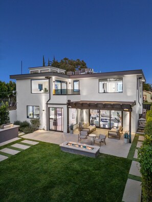 A modern two-story house with a patio area, outdoor seating, and a fire pit.