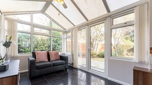A conservatory with a grey sofa, large windows, and a ceiling fan. - Large Home near Edgbaston Stadium, UOB & QE hospital sleeps 6 (Birmingham)