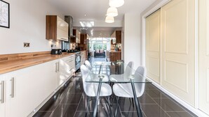 A modern kitchen with a glass dining table and chairs, stainless steel appliances, and pendant lighting. - Large Home near Edgbaston Stadium, UOB & QE hospital sleeps 6 (Birmingham)