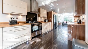 A modern kitchen with stainless steel appliances, wooden cabinets, and a large island with a sink. - Large Home near Edgbaston Stadium, UOB & QE hospital sleeps 6 (Birmingham)