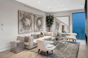 Relax in a stylish living room with a neutral-toned sofa, glass coffee table, and modern armchair, surrounded by abstract art and lush greenery.