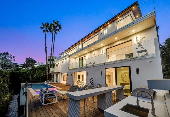 A modern two-story house with a swimming pool, outdoor seating, and a balcony.