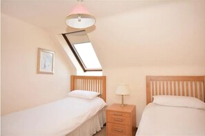 Two single beds with bedside tables and lamps, a framed picture, and a skylight.