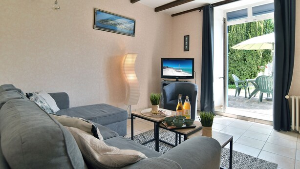 A living room with a sofa, a TV, a table with drinks, and a view of the outdoors. - L'Armoricaine (Cancale)