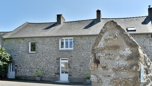 A stone building with a white door and windows, a paved driveway, and a stone wall in the foreground. - L'Armoricaine (Cancale)