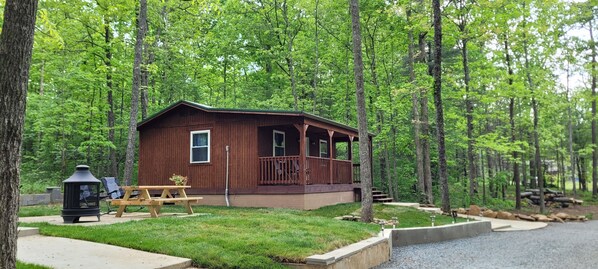 Eine Hütte mit Veranda, Picknicktisch und Feuerstelle in einer Waldlandschaft.