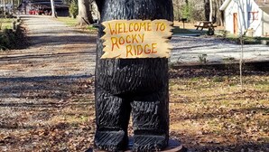 Eine Holzstatue eines Bären mit einem Schild, auf dem 'Welcome to Rocky Ridge' steht.