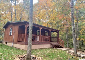 Eine Holzblockhütte mit Veranda und Treppe, umgeben von Bäumen mit Herbstlaub.