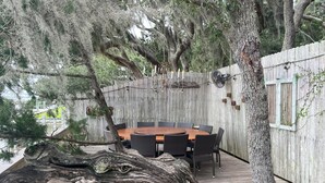 Eine Holzterrasse mit rundem Tisch und Stühlen, umgeben von Bäumen und einem Holzzaun.