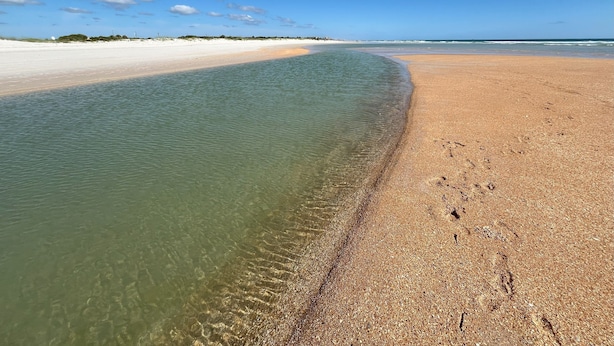 Ein Strand mit klarem, seichten Wasser und einem sandigen Ufer.