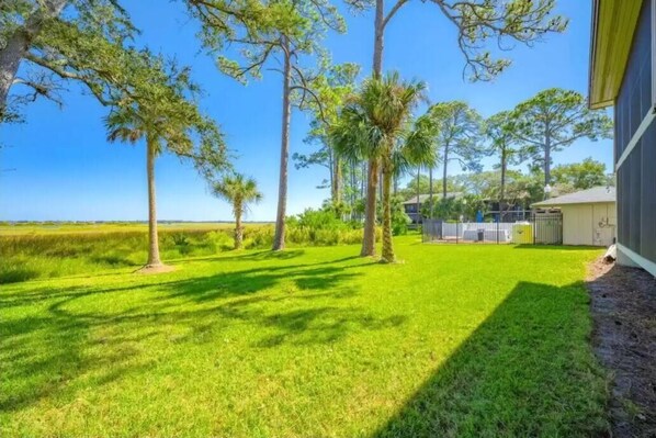 A well-maintained lawn with tall trees and a clear view of the ocean.