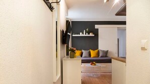 A narrow hallway with a white wall, a wooden floor, a white cabinet, and a gray sofa with yellow and gray cushions. - 2-Bedroom-Apartment in Berlin-Kreuzberg (Berlin)