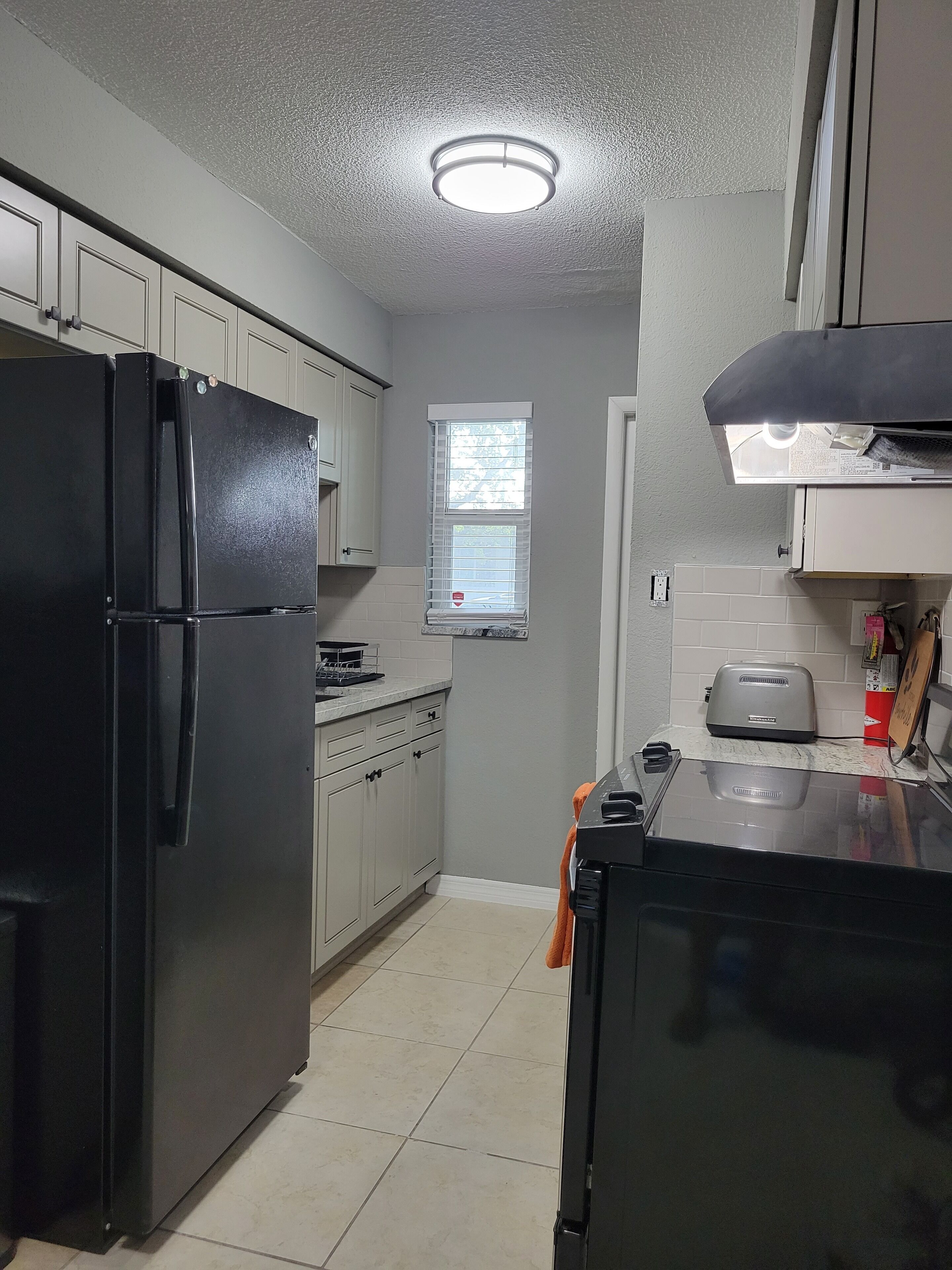 Una cocina compacta con un refrigerador negro, un tostador y una ventana con persianas.