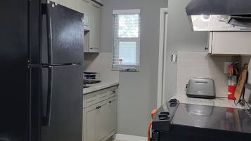 Una cocina compacta con un refrigerador negro, un tostador y una ventana con persianas.