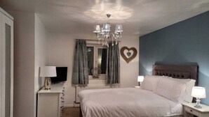 A bedroom with a bed, bedside tables, a TV, a chandelier, curtains, and a heart-shaped decoration on the wall. - Charming Wentworth Lodge With Countryside Views (Rotherham)