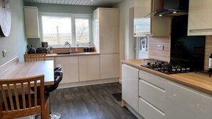 A modern kitchen with a wooden dining table, white cabinets, and a black stove. - Charming Wentworth Lodge With Countryside Views (Rotherham)