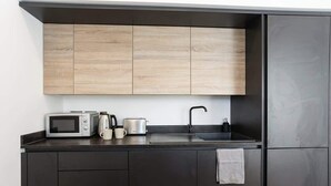 Una cocina compacta con muebles oscuros, microondas, tostadora, hervidor y un lavabo.