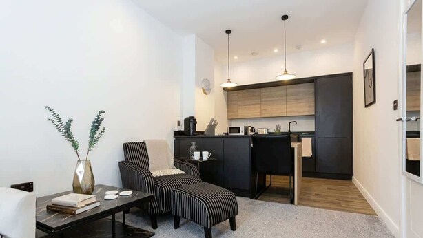 Un espacio habitable compacto con kitchenette, una zona de comedor con sillas a rayas y un pequeño rincón de estar.