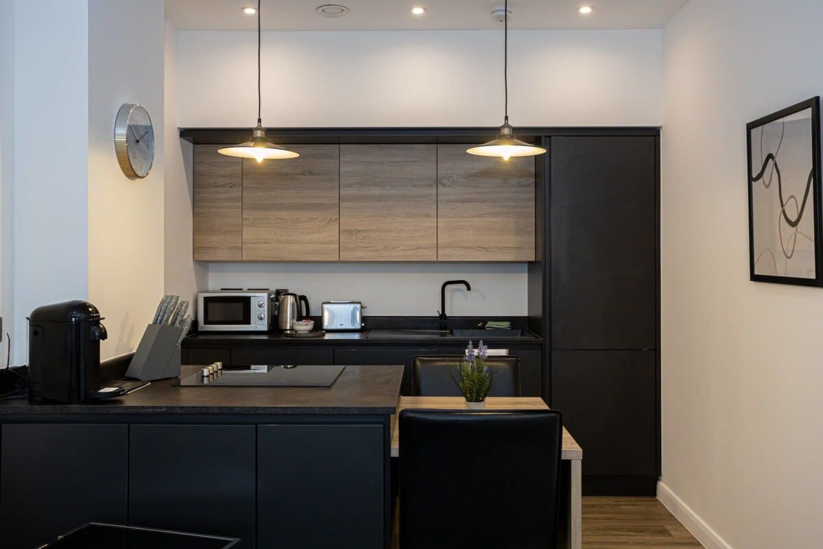 Une cuisine moderne avec des meubles de rangement aux couleurs foncées, un four à micro-ondes, une machine à café et des luminaires suspendus.