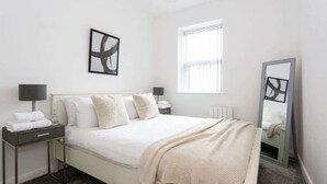 Un dormitorio con una cama, mesitas de noche, una ventana y un espejo.