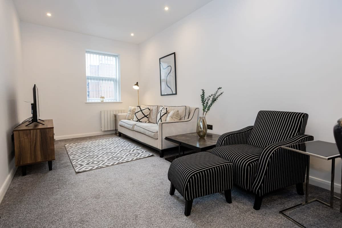 A modern living room with a sofa, two striped armchairs, a coffee table, a side table, a floor lamp, and a framed artwork on the wall.