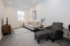 A modern living room with a sofa, two striped armchairs, a coffee table, a side table, a floor lamp, and a framed artwork on the wall.
