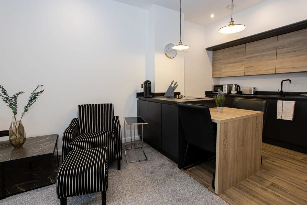 A modern kitchen with a wooden countertop, black chairs, a small dining table, and a hanging light fixture.