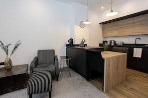 A modern kitchen with a wooden countertop, black chairs, a small dining table, and a hanging light fixture.