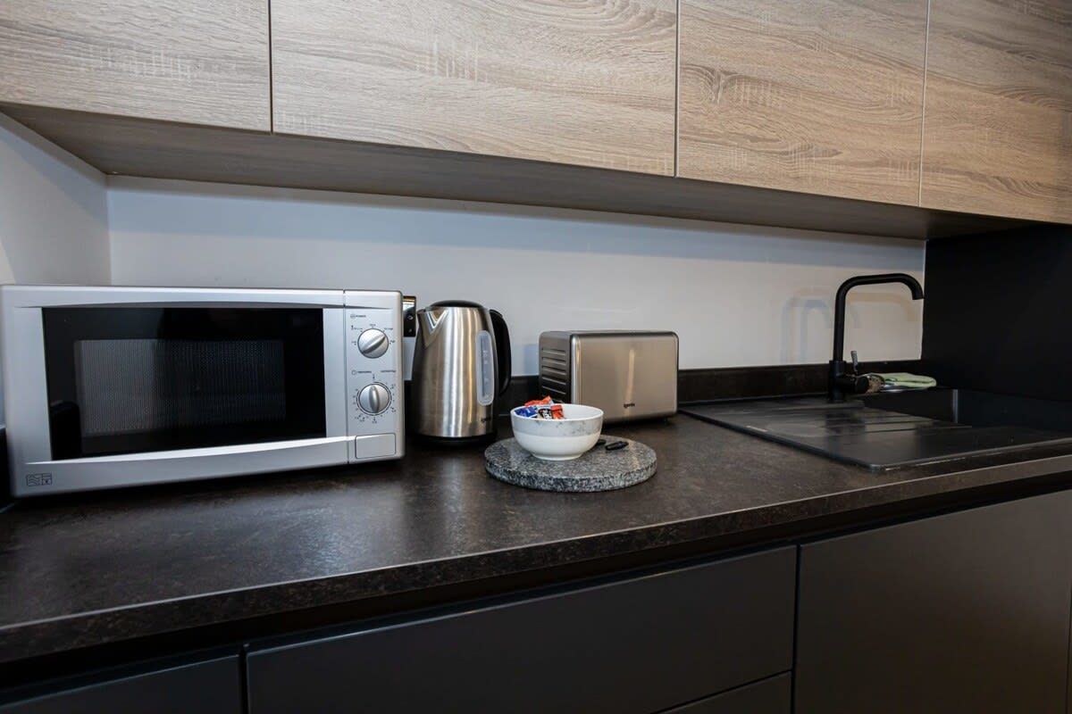 A modern kitchen with a microwave, toaster, kettle, and a bowl on the counter.