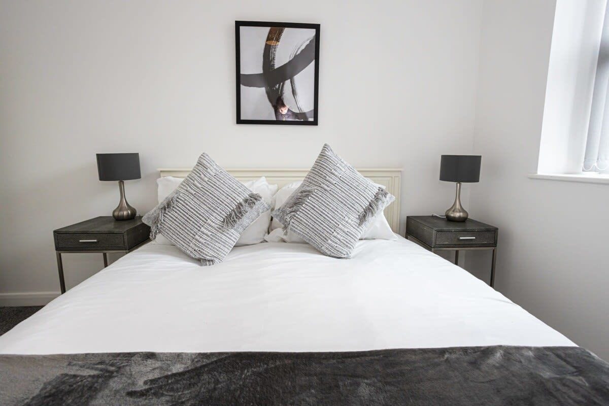 A neatly made bed with two pillows, two bedside tables with lamps, and a framed abstract artwork on the wall.