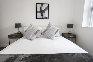 A neatly made bed with two pillows, two bedside tables with lamps, and a framed abstract artwork on the wall.