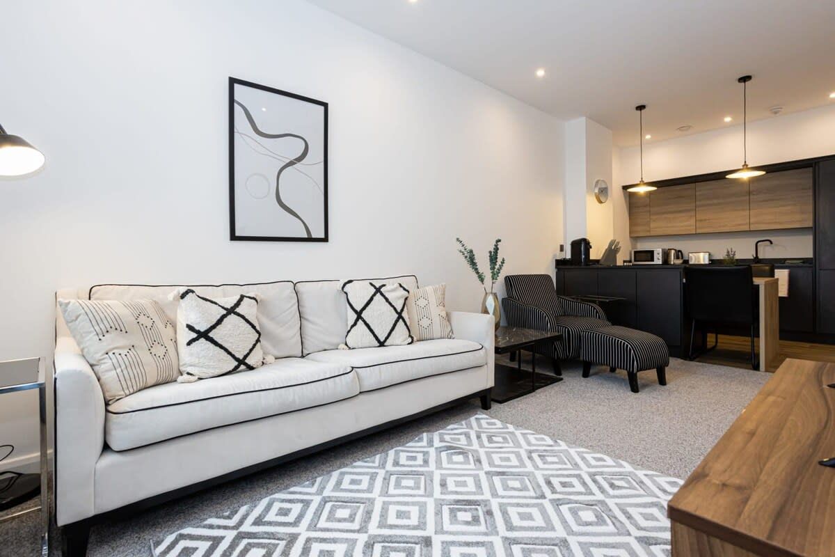 A modern living room with a sofa, ottoman, and a patterned rug.