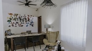 Una sala de estar moderna con comedor, que presenta un gran cuadro de arte geométrico, un ventilador de techo y un amplio ventanal con cortinas traslúcidas.