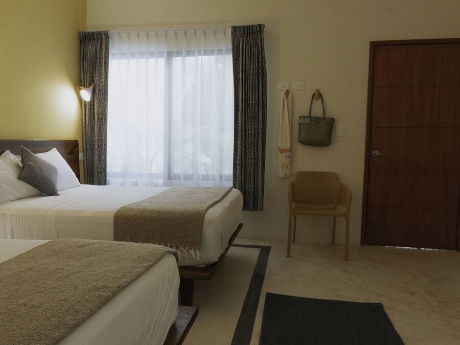 Ein Hotelzimmer mit zwei Betten, einer Holztür, einem Stuhl und einem Fenster mit Vorhängen.