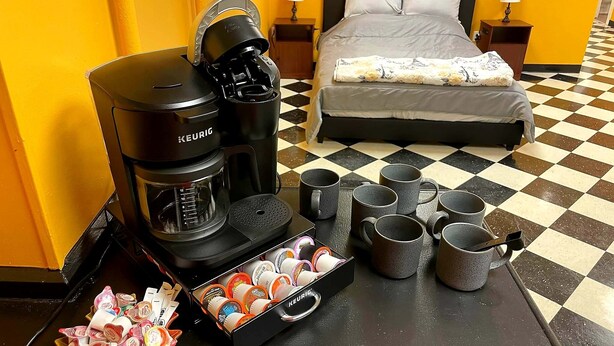 A hotel room with a bed, a coffee maker, and several mugs on the floor.