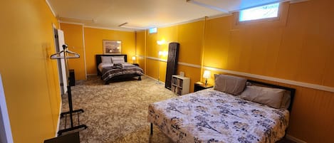 A hotel room with a large bed, a smaller bed, a wardrobe, a mirror, a shelf with books, and a window with blinds.