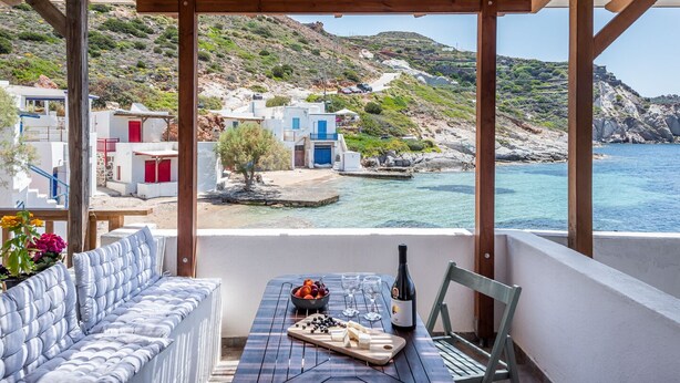 A balcony with a table set for dining, overlooking a coastal village with white buildings and a clear view of the sea. - ECO SIRMA FLARIS (Milos)