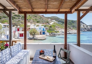 A balcony with a table set for dining, overlooking a coastal village with white buildings and a clear view of the sea. - ECO SIRMA FLARIS (Milos)