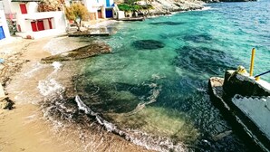 A coastal area with clear turquoise waters, sandy beach, and buildings with red and white facades. - ECO SIRMA FLARIS (Milos)