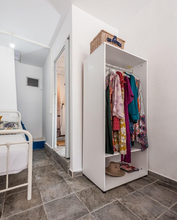 A hallway with a white wardrobe, a bed with a white metal frame, and a tiled floor. - ECO SIRMA FLARIS (Milos)